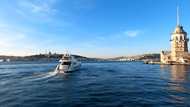 A luxury yatch sets sail in the Bosphorus Strait. As it gracefully navigates through the current, the Maiden's Tower comes into view. While continuing its journey, seagulls greet it. The sounds of waves and seagulls can be heard.