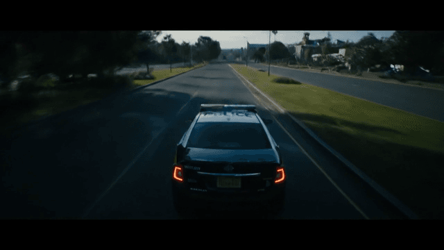 the camera hangs back and ascends to a high angle. As a police car speeds fowards with it's lights on entering the frame. The camera finishes at rear tracking shot.